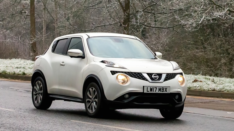 Белый Nissan Juke на дороге с легким снегом и деревьями