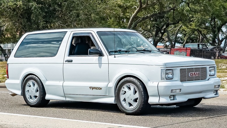 Белый GMC Typhoon изображен на фоне дубовых деревьев.
