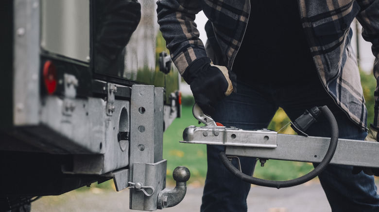 Человек, пытающийся прикрепить трейлер автофургона к буксируемой зацепке транспортного средства