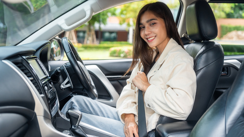 Молодая женщина на сиденье водителя улыбается и надевая ремень безопасности