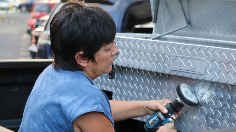 Женщина полирует алюминиевый набор инструментов, сидя в кровати грузовика.