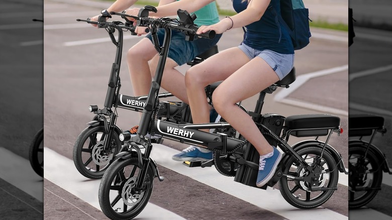 Женщина, которая катается на электронном велосипеде с собакой в ​​ящике спереди.