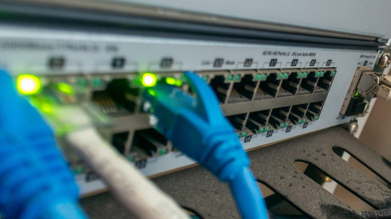 Крупным планом изображение современного коммутатора Ethernet с подключенными сетевыми кабелями. Освеченные индикаторы сигнализируют о активных соединениях в настройке сети данных.