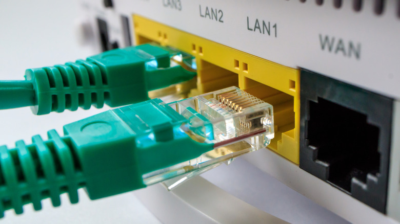 Задняя часть маршрутизатора показывает порты Ethernet. Один зеленый кабель Ethernet врезается в порт. Другой находится в процессе просачивания.