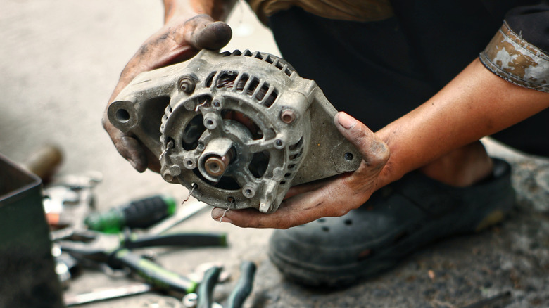 Механик с грязными руками, держащий изношенный генератор