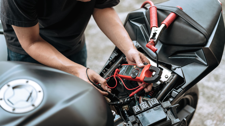 Человек осматривает мотоциклетную батарею на обочине дороги