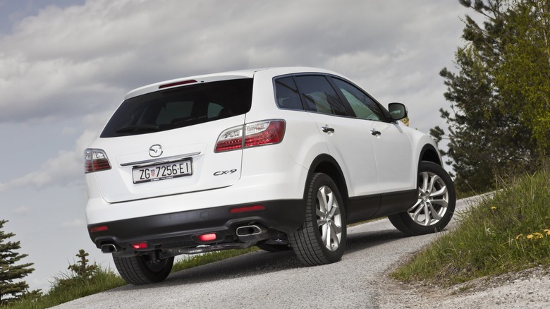 Белый внедорожник Mazda CX-0 идет в гору на гравийной дороге