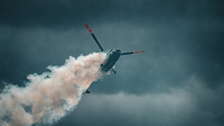 Вертолет выполняет воздушный трюк, затягивая дым к облачному небу