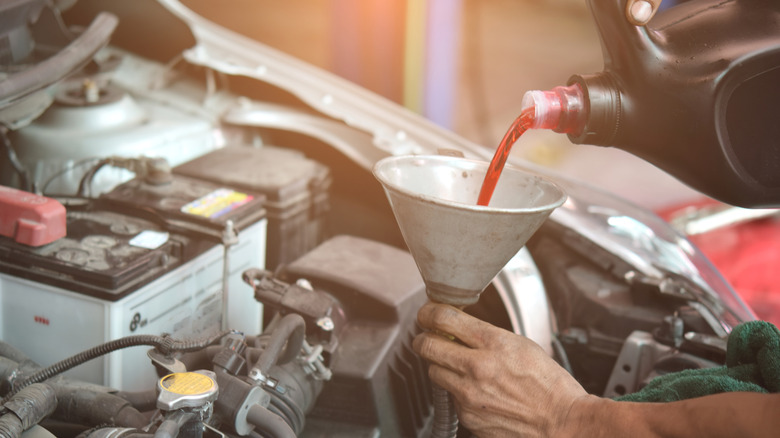 Трансмиссионное масло заполняет автомобильный двигатель с помощью металлического конуса.