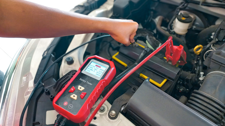 Автомобильный механик тестирует аккумулятор с помощью цифрового электронного тестера батареи