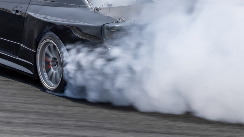 Черная машина делает выгорание с курящими задними колесами