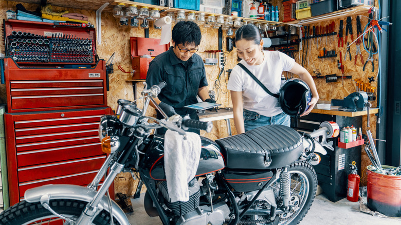 Два человека осматривают мотоцикл, стоящий в мастерской