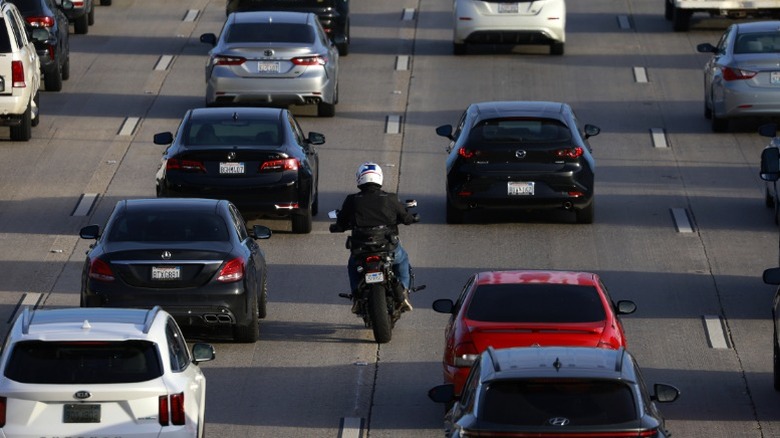 Мотоциклист -переулок расщепляется на оживленном калифорнийском шоссе
