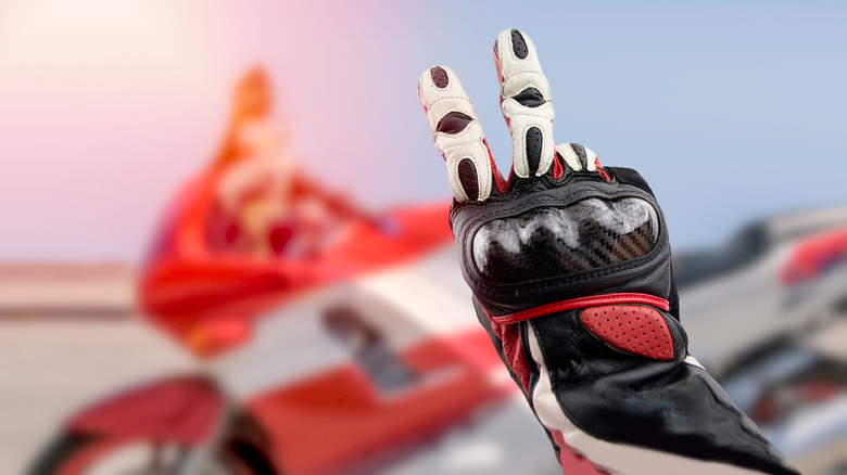 Байкер в перчатках, используя V Знак с велосипедом, припаркованным позади