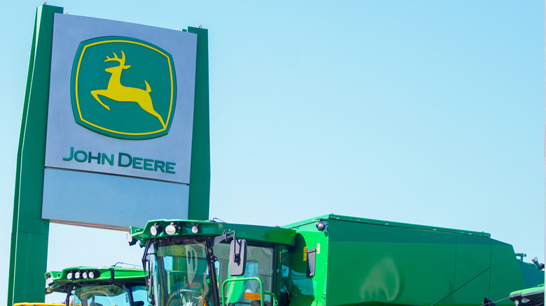 Вывеска дилерского центра John Deere рядом с несколькими зелеными тяжелыми механизмами