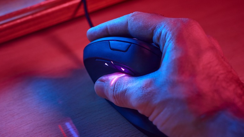 Мужская рука, держащая черную вертикальную мышь на стойке RGB, освещающего RGB
