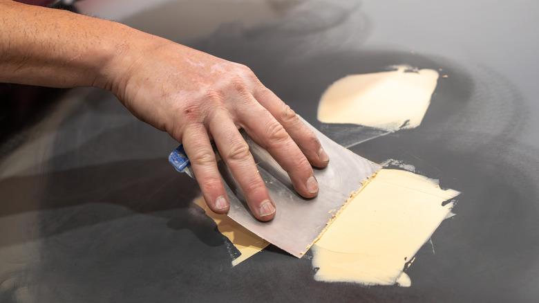 Человек применяет наполнитель тела на автомобильный капюшон