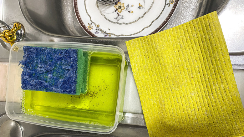 Грязная скраба и губка на краю раковины блюда