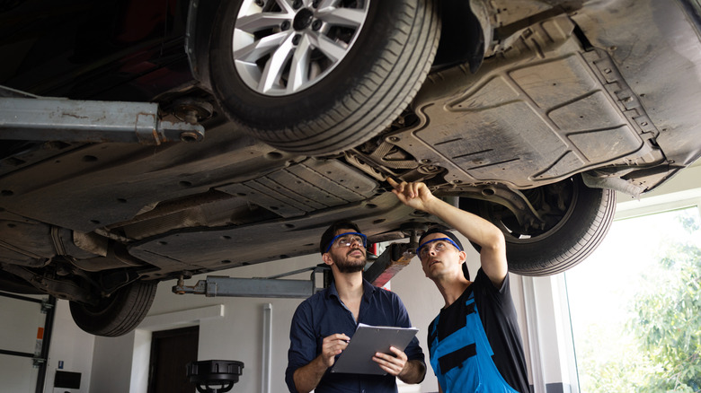 Двое мужчин осматривают нижнюю часть автомобиля