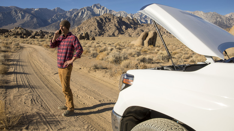 Человек, призывающий к помощи рядом с сломанным транспортным средством в пустыне