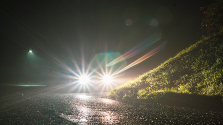 Автомобиль с высокими лучами, припаркованными рядом с небольшим холмом ночью