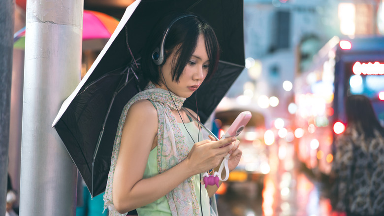 Человек, одетый в наушники Y2K, используя старый розовый флип-телефон.