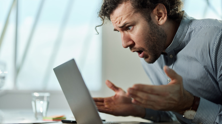 Паникованный и шокированный человек, глядя на свой ноутбук