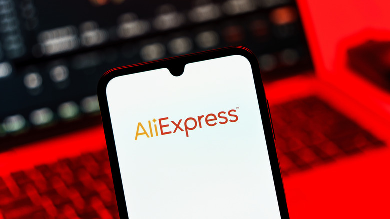 Телефон с логотипом Aliexpress и ноутбуком на фоне