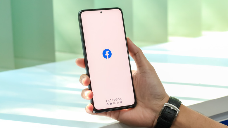 Человек держит телефон, который отображает логотип TE Facebook на белом фоне.