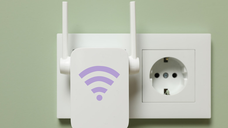 Новый современный ретранслятор с символом Wi-Fi, подключенным к розетку на светло-зеленой стене