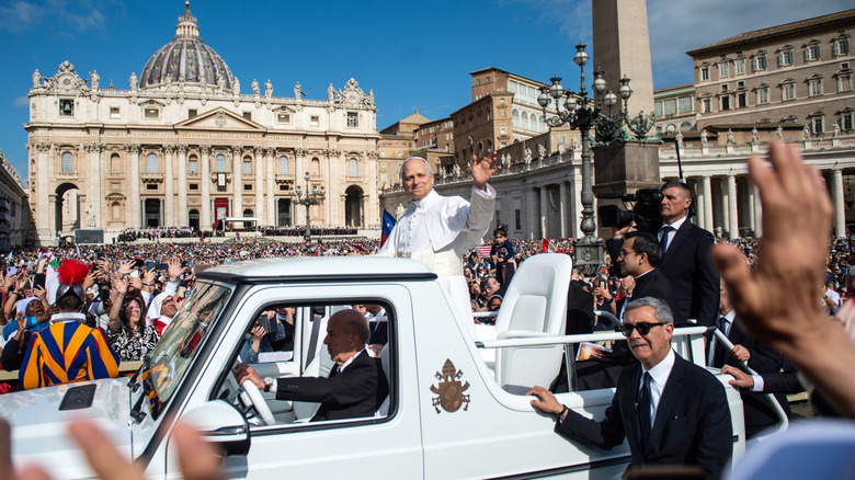 Папа Лео XIV размахивает от своего автомобиля.