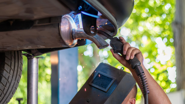 Механик обслуживает выхлопную систему сварщиком