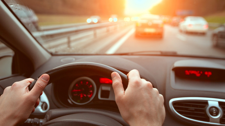 Водитель, использующий обе руки, чтобы схватить колесо, во время проезжая по шоссе.