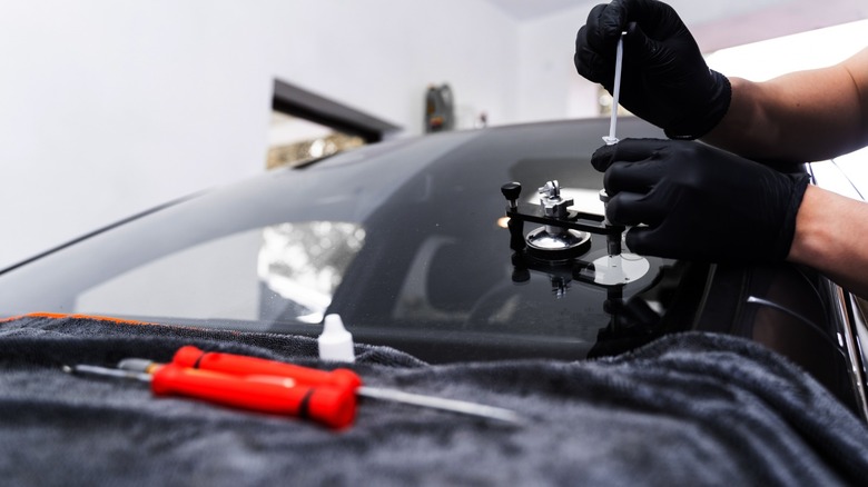 Техник, ремонтирующий трещину лобового стекла, используя инструмент