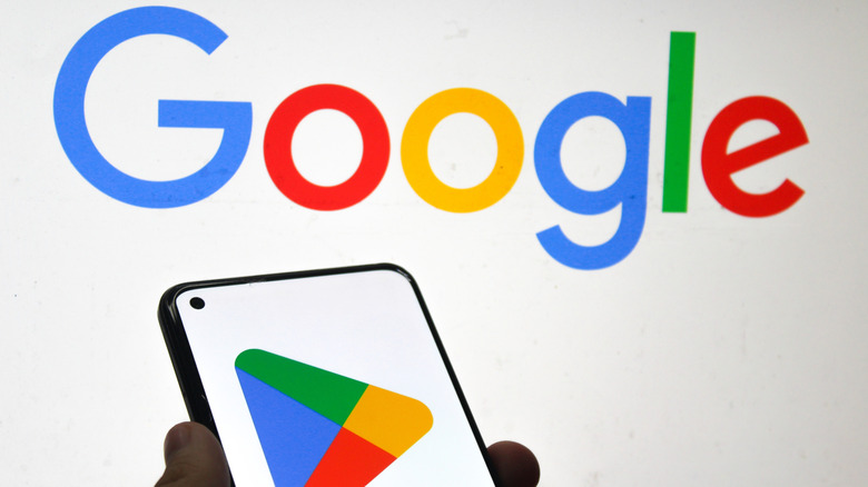 Google Play Store Logo на экране мобильного телефона с логотипом компании Google в фоновом режиме