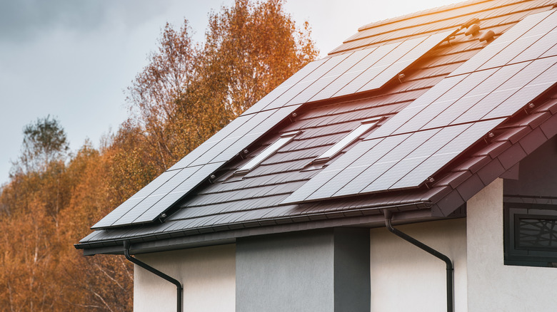 Фото современного дома с солнечными батареями и осенними деревьями.