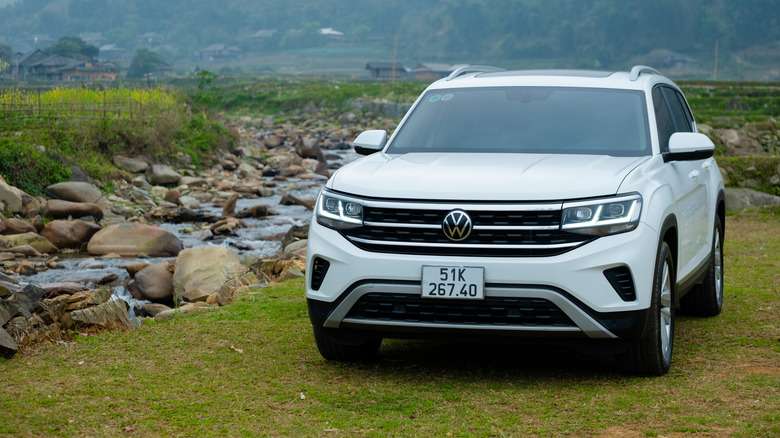 Белый Volkswagen Teramont припаркован возле потока на зеленой траве.