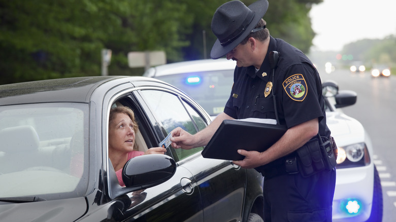 Женщина в черной машине, передающая свою лицензию полицейскому после того, как ее остановили