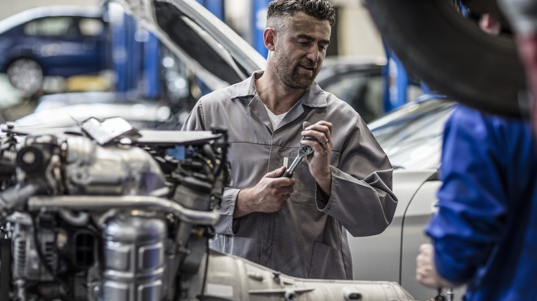 Механики обслуживают полную трансмиссию, удаленную из автомобиля в профессиональном магазине