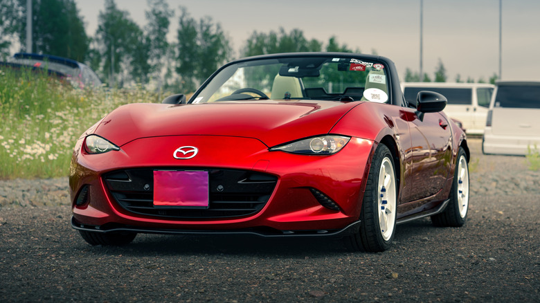 Igora Drive, Red Mazda MX-5 Convertible Car, припаркованный на гравии с белыми фургонами и зелеными деревьями на заднем плане
