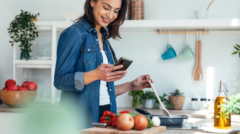 женщина готовит на кухне, используя свой смартфон