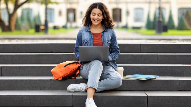 Женщина сидит на ступеньках в колледже и делает домашнее задание