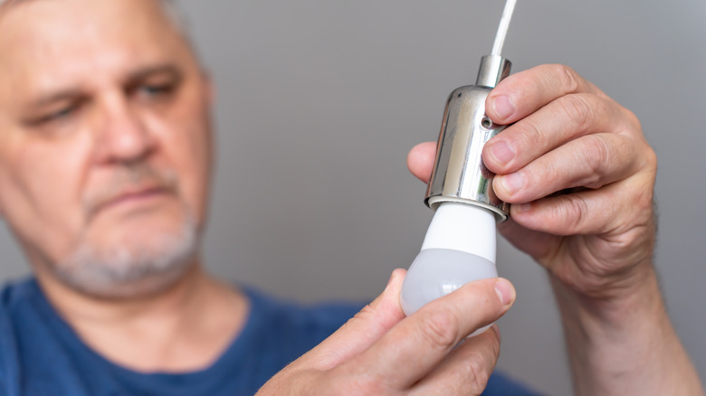 Мужчина вставляет лампочку в розетку.