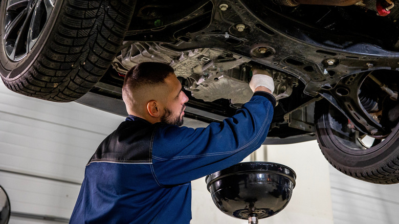 Механик сливает масло из двигателя автомобиля