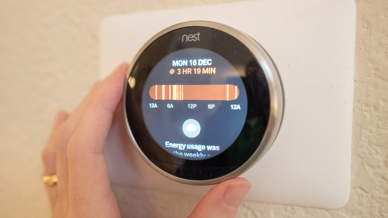 Крупный план руки, регулирующей умный термостат Nest.