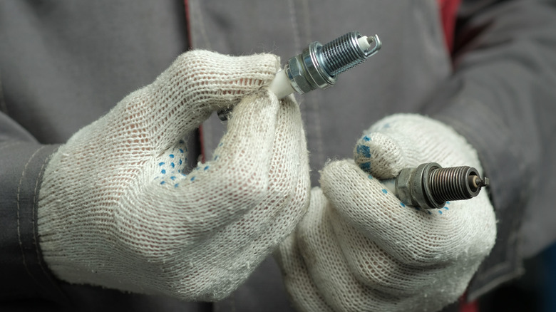 Техник по обслуживанию держит в каждой руке новую и старую свечу зажигания.