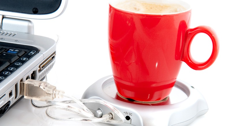 Белый USB-подогреватель для кружек, подключенный к ноутбуку, с красной чашкой на нем