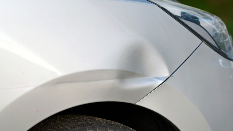 Крыло белого автомобиля с вмятиной