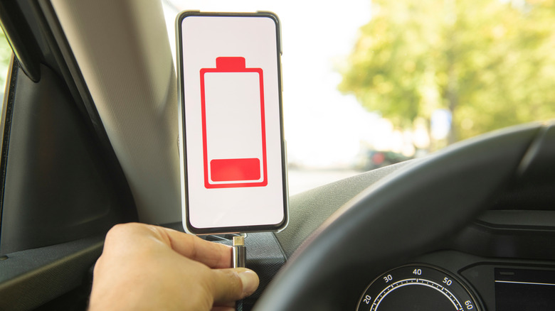 человек в машине подключает шнур USB-C к смартфону с индикацией низкого заряда батареи