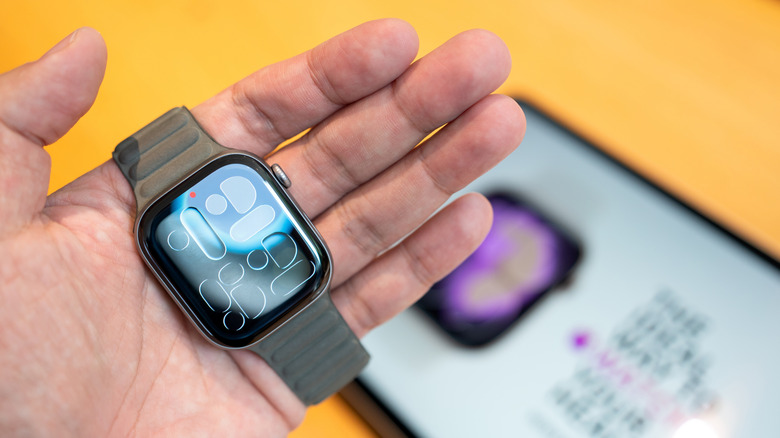 Человек, держащий Apple Watch на ладони, на фоне размытого iPad